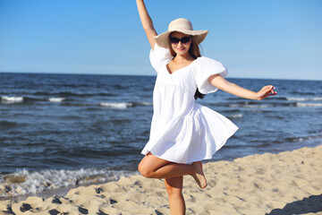 Happy blonde woman having fun on the ocean beach in a white dress and sunglasses