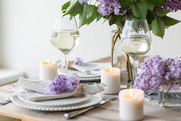 Beautiful table decor for a wedding dinner with a spring blooming lilac flowers. Celebration of a special holiday marriage event. Fancy white plates, wineglasses, candles. Countryside style