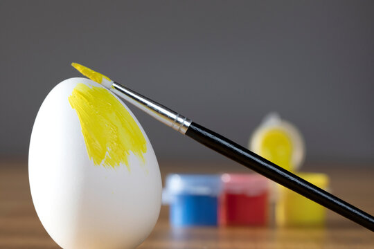rough brush is painting a fragile easter egg with Yellow color, prepering for Holiday Happy Easter concept closeup