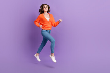 Full length photo of sweet cute woman dressed orange jumping high running fast empty space isolated...