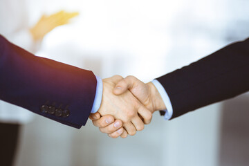 Business people shaking hands at meeting or negotiation, close-up. Group of unknown businessmen and a woman standing in a sunny modern office. Teamwork, partnership and handshake concept