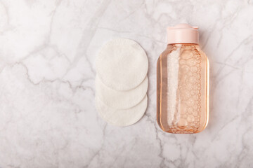 Micellar cleansing water and cotton pads on a marble background. Facial cleansing or makeup remover cosmetic bottle in bathroom. Skin care concepts. Cleansing the face of makeup and skin sebum.