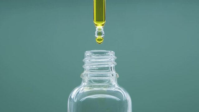 Oil drops from pipette into glass bottle.  Cosmetics oils based on natural ingredients. Close up glasses bottle with natural essential oil on gray background. 