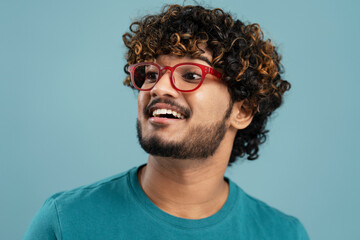 Obraz premium Portrait of smiling confident Indian man wearing red stylish eyeglasses looking away isolated on blue background 