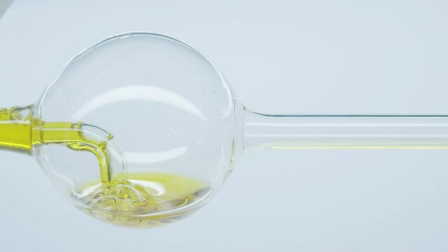 Yellow natural oil flows through laboratory spherical glass tube. Cosmetic natural oil. Filtration process of natural essential oils. Cosmetics oils based on natural ingredients.