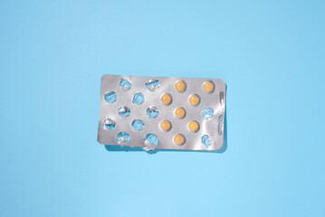 Round yellow pills in a blister pack on a blue background, top view