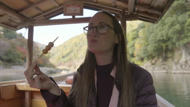 This video shows a tourist female eating a mochi snack on a Japanese boat as she sails through scenic waters.
