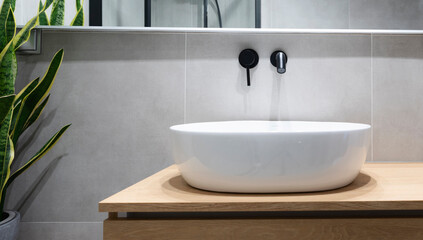 Ceramic wash basin on the wooden countertop and stylish tap on the wall. Minimalism and modern design in interior of bathroom.
