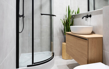 Interior of bathroom with ceramic sink on the wooden cabinet, mirror on the wall and shower. Modern room with minimalism.