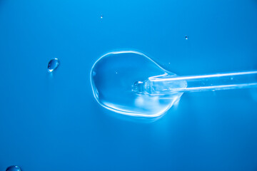Water bubbles with cosmetic liquid drops of serum on a blue background of a laboratory glass...