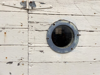 metal and glass port hole window in hinged white, rough wood door at shipyard