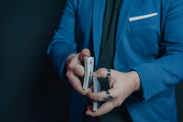 Close-up image of a young magician in the dark holding a deck of cards with both hands and putting...