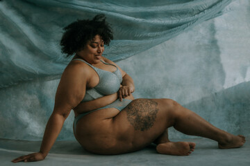 portrait of a plus size afro indigenous person sitting sideways on floor looking down smiling
