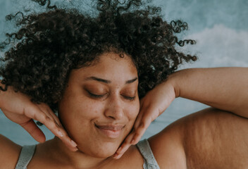 close up portrait of a plus size afro indigenous person's face with hands on cheeks
