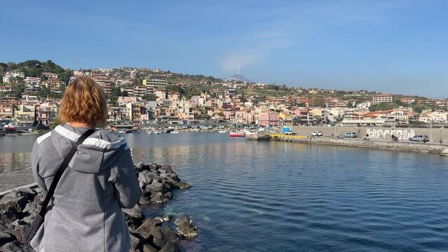Tourist woman takes pictures with a smartphone of the sea and volcano. Woman looking at the sea and volcano Etna in Sicily, Acitrezza