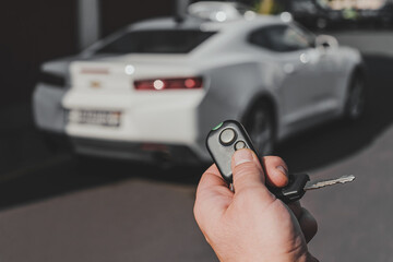 The man opens the car with a keychain, in the background is a white car.