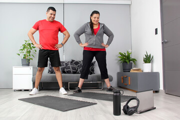 Latino adult couple of man and woman exercise at home taking online class they see the laptop in...