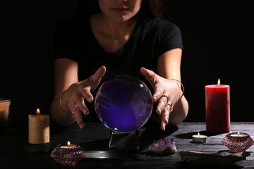 Fototapeta na wymiar Soothsayer using crystal ball to predict future at table in darkness, closeup