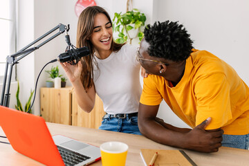 Two young millennial content creator students having fun recording radio podcast. Young african man live streaming online radio show with pretty female friend. Creativity and trend concept