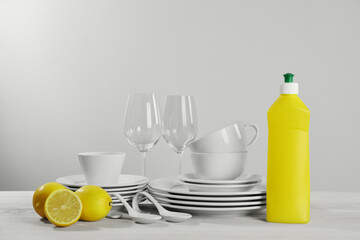 Set of clean tableware, glasses, dish detergent and lemons on white wooden table against light background