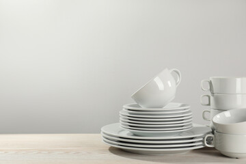 Set of clean dishware on white wooden table against light background. Space for text