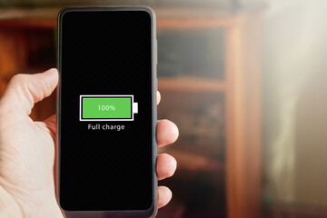 Close up of male hand holding smartphone with full battery icon on the screen indicating that battery level is at one hundred percent. Full charged battery level.