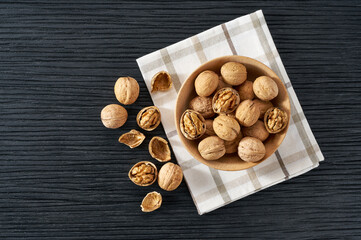 walnuts in wooden bowl on black table with copy space. Top view