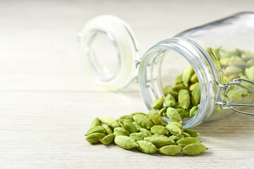 green cardamom pods spill out of a glass storage jar  on a white wooden background, selective focus.