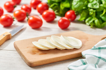 sliced Italian cheese mozzarella buffalo with cherry tomatoes and green fresh organic basil on a kitchen table.