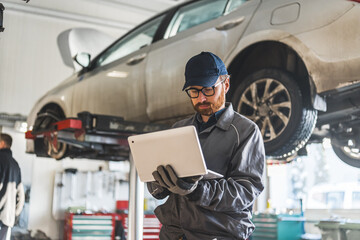 young serviceman checking car diagnostics with a laptop, car in the background medium shot. High quality photo