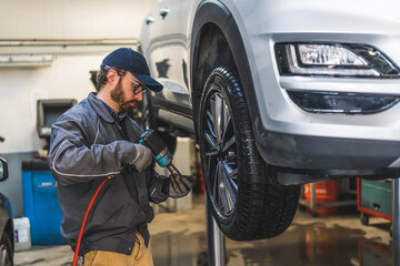 professional mechanic with glasses and uniform working on a car wheel, auto repair shop. High quality photo
