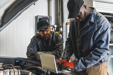 Fototapeta na wymiar two multiracial mechanics checking car diagnostics with a laptop, medium shot car repair concept. High quality photo