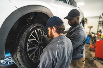 Fototapeta na wymiar medium back shot of two mechanics changing the wheel on a car, car repair shop. High quality photo