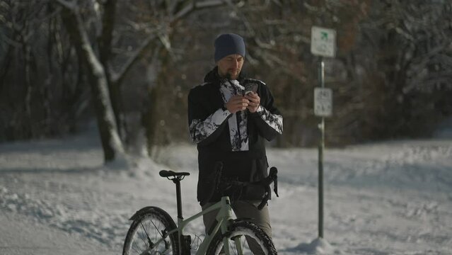 Navigation, GPS positioning, routing, offline map in a smartphone. Male cyclist stopped while cycling in winter in snow to check messages and direction of the journey. Bicycle rides in snowy weather. 