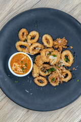 Overhead view of tempting appetizer of breaded calamari rings with dipping sauce and served on a small plate