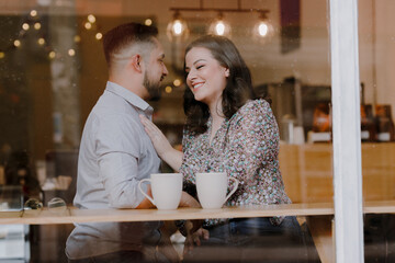 Affectionate couple having a date in a coffee shop - Hispanic couple laughing while drinking coffee