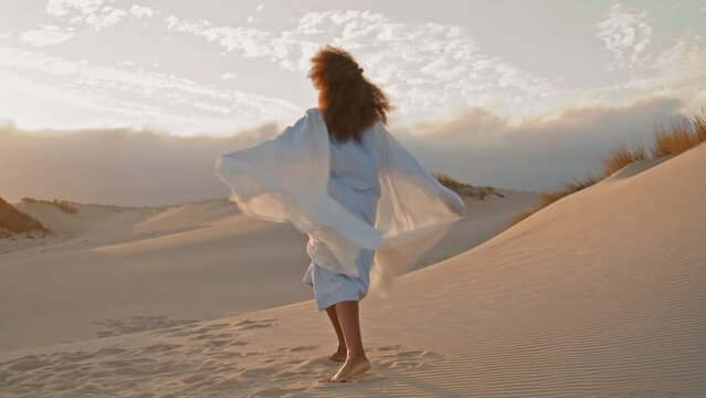 Woman waving fluttering cloth dancing on dunes summer sunset. Girl performing.