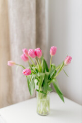 A bouquet of Pink tulips in a glass vase stands in a bright room. Background for Valentine's Day. Gift for Mother's Day or Women's Day. Spring background