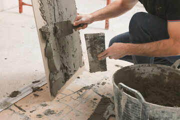 Worker spreading adhesive mix over tile with spatula, closeup
