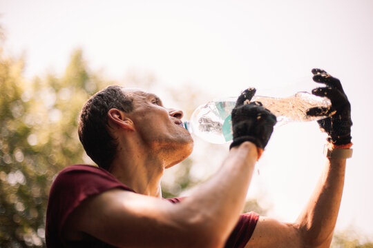 Thirsty man farmer drinking water from bottle in the garden during summer heat