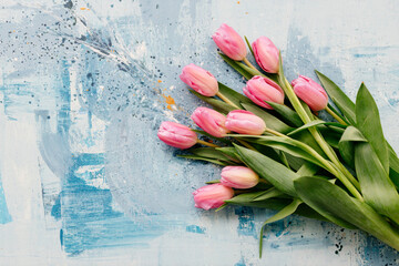 A bouquet of pink fresh tulips lies on a blue and turquoise scenic art background. Valentine's Day....