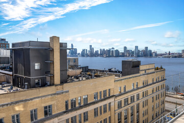 View from lower Manhattan looking over a brick building across the Hudson to the Jersey City skyline, sunny with clouds, nobody