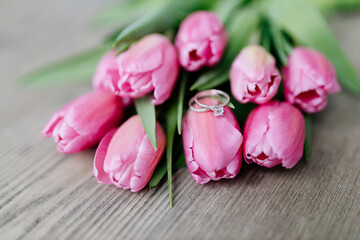 Pink tulips and engagement rings with diamonds lie on a wooden background. Background for Valentine's Day. Gift for Mother's Day or Women's Day