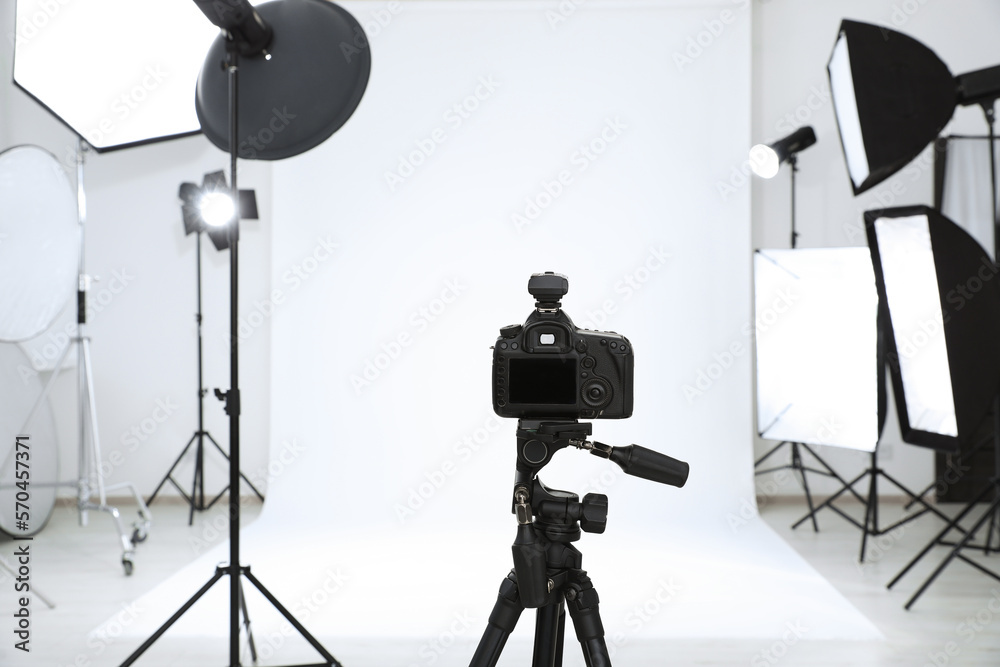 Wall mural Tripod with camera and professional lighting equipment in modern photo studio