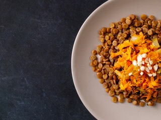 Homemade vegan stew Lentil with carrot, onion and garlic on plate on black background. Healthy vegetarian lifestyle. Diet diabetic menu. Top view, copy space