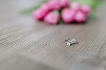 Pink tulips and engagement rings with diamonds lie on a wooden background. Background for Valentine's Day. Gift for Mother's Day or Women's Day