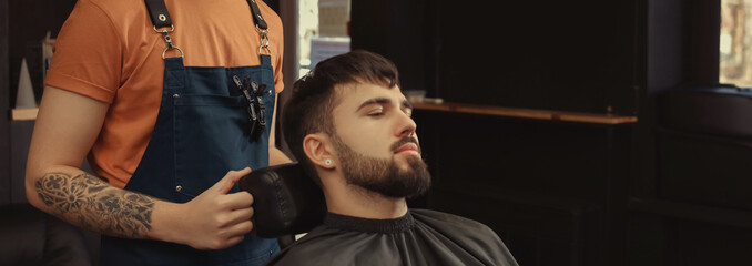 Fototapeta na wymiar Professional hairdresser working with bearded client in barbershop, space for text. Banner design