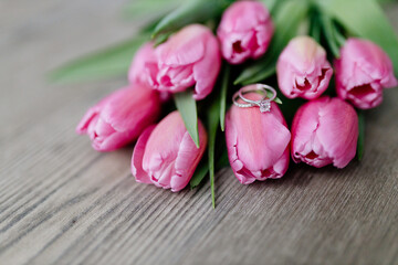 Pink tulips and engagement rings with diamonds lie on a wooden background. Background for...