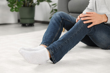 Man suffering from leg pain on white carpet at home, closeup