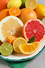 Plate with different citrus fruits and fresh leaves on light grey table, closeup